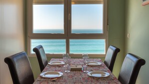 A dining table set for four with a view of the ocean through large windows.