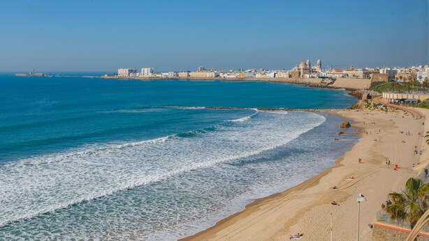 A coastal cityscape with a sandy beach, a rocky shoreline, and a clear blue sky.