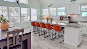 Een moderne keuken met een groot eiland, barkrukken en een eethoek met een houten tafel en stoelen.