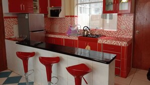 A kitchen with red cabinets, a black countertop, and a tiled backsplash. There are three red bar stools and a kettle on the stove. - Apartment Rosa elena b&b (A)Luz natural capacity 9 people in Cusco-Peru (Cusco)