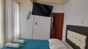 A hotel room with a teal bedspread, white pillows, a black TV mounted on the wall, and a wooden door leading to a bathroom. - Apartment Rosa elena b&b (A)Luz natural capacity 9 people in Cusco-Peru (Cusco)