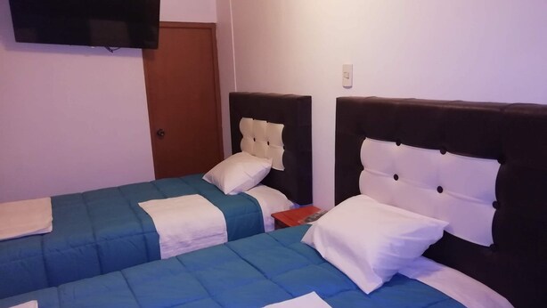 Une chambre d’hôtel avec deux lits, chacun recouvert d’une couette bleue et blanche, dotés d’une tête de lit en bois et d’une petite table de chevet sur laquelle se trouve un objet rouge.