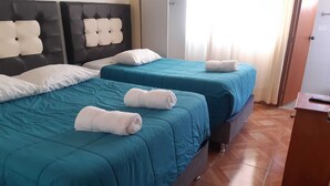 Une chambre d’hôtel avec deux lits, chacun agrémenté de draps turquoise et d’oreillers blancs. Des serviettes sont posées sur les lits, et la chambre est dotée d’un plancher en bois.