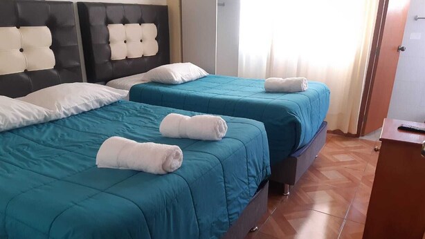 A hotel room with two beds, each with teal bedding and white pillows. There are towels on the beds, and the room has a wooden floor. - Apartment Rosa elena b&b (A)Luz natural capacity 9 people in Cusco-Peru (Cusco)