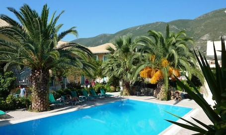 A pool area with palm trees, lounge chairs, and a mountain backdrop.