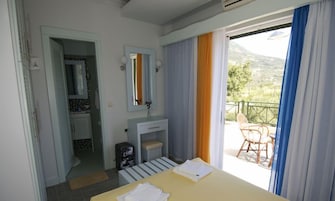 Habitación de hotel con cama, baño, lavamanos pequeño y balcón con una silla.