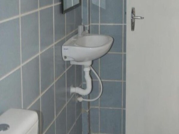 A bathroom with a white pedestal sink, a toilet, and tiled walls.