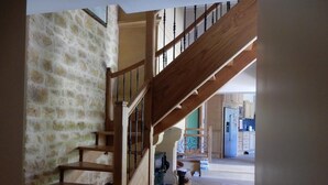 A wooden staircase with a stone wall on one side, leading to a kitchen area with cabinets and appliances. - Le Hibou Heureux (Castels et Bézenac)
