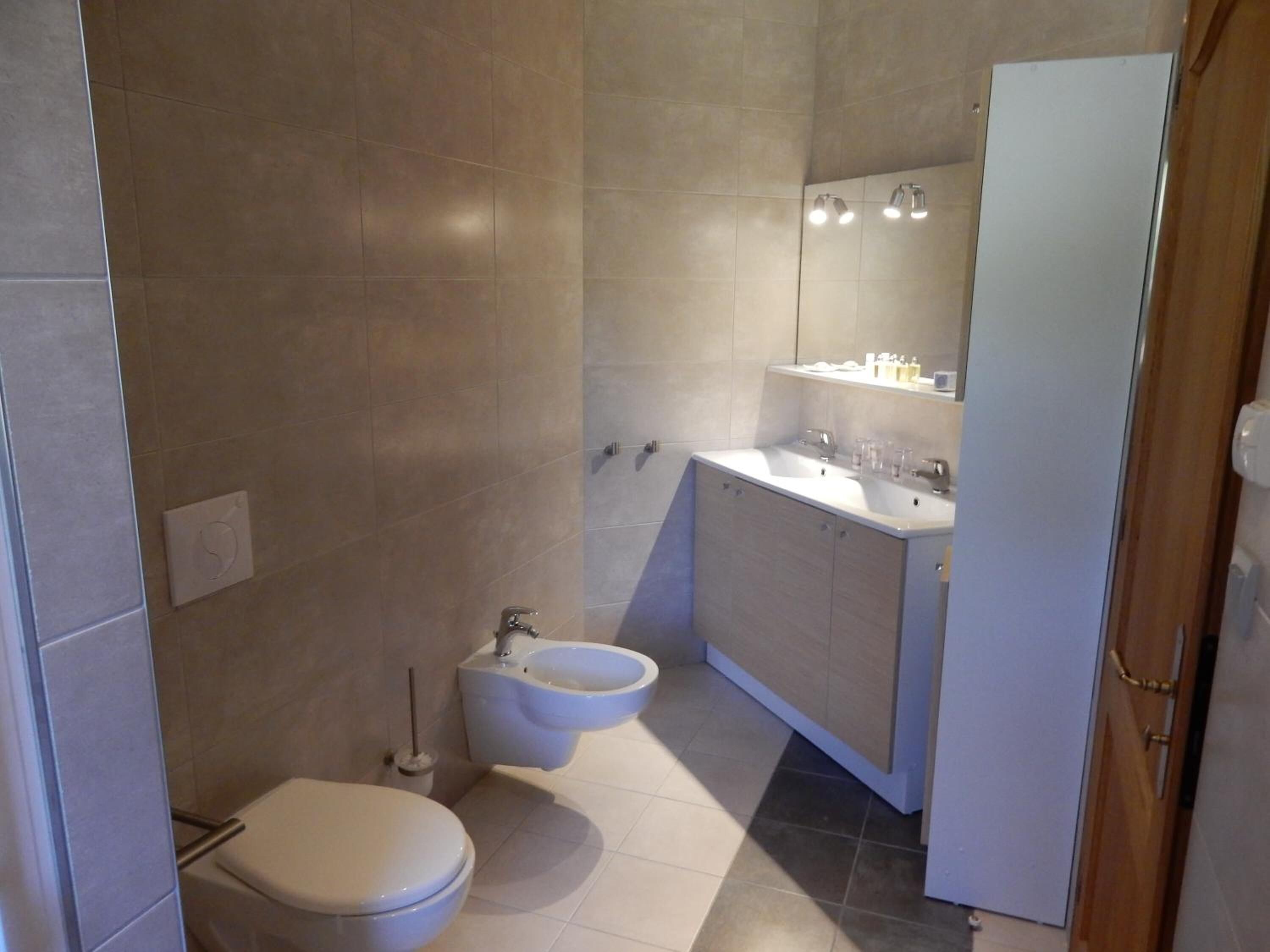 Un baño moderno con dos inodoros, un bidé, un lavabo y un espejo.