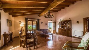 A spacious living room with a wooden ceiling, a dining area with chairs and a table, a sofa, and a cabinet. - Rural Apartment Lledoner de Son Amer (Felanitx)