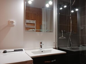 A modern bathroom with a large mirror, a white sink, and a glass-enclosed shower area.