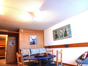 A cozy room with a wooden wall, a sofa with patterned cushions, a small round table, and a painting of animals.