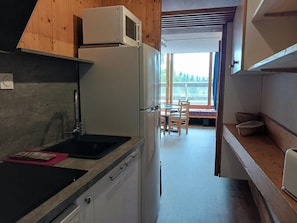 A compact kitchen with a refrigerator, microwave, and sink. There is a dining area with a table and chairs visible through an open doorway.
