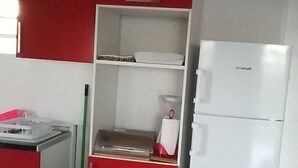 Pieni, käytännöllinen keittiö, jossa on punaiset kaapit, valkoinen jääkaappi ja pieni roskakori.