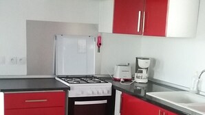 Pieni, käytännöllinen keittiö, jossa on punaiset kaapit, valkoinen jääkaappi, liesi ja pesuallas.