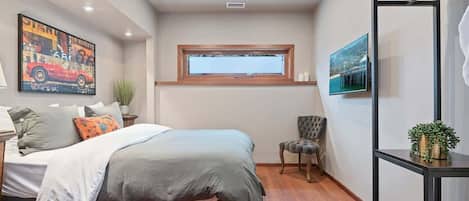 Ein Schlafzimmer mit einem Bett, einem Fenster, einem Sessel und einem Fernseher an der Wand.