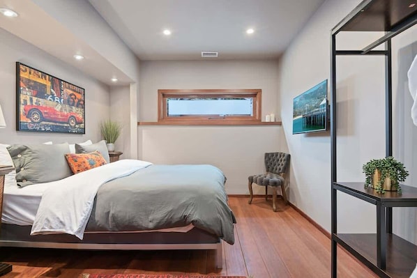 A bedroom with a bed, a window, a chair, and a TV on the wall.