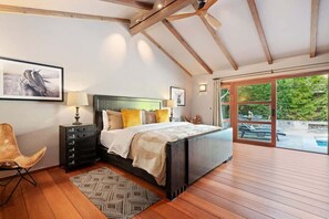 A bedroom with a large bed, wooden flooring, a nightstand, a chair, and a view of an outdoor swimming pool.