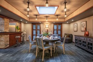 A dining area with a round table, chairs, a bar with stools, and a view through a skylight.