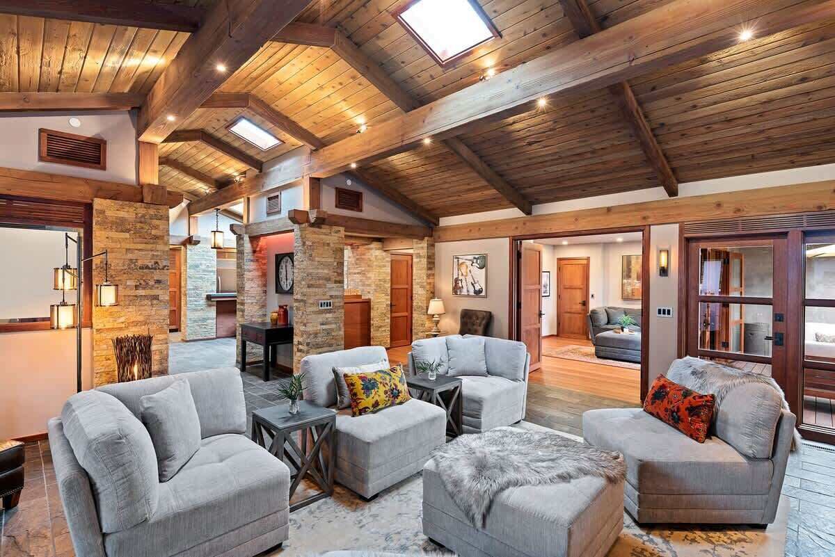 A spacious living area with multiple seating options, a stone accent wall, and a high wooden ceiling with skylights.