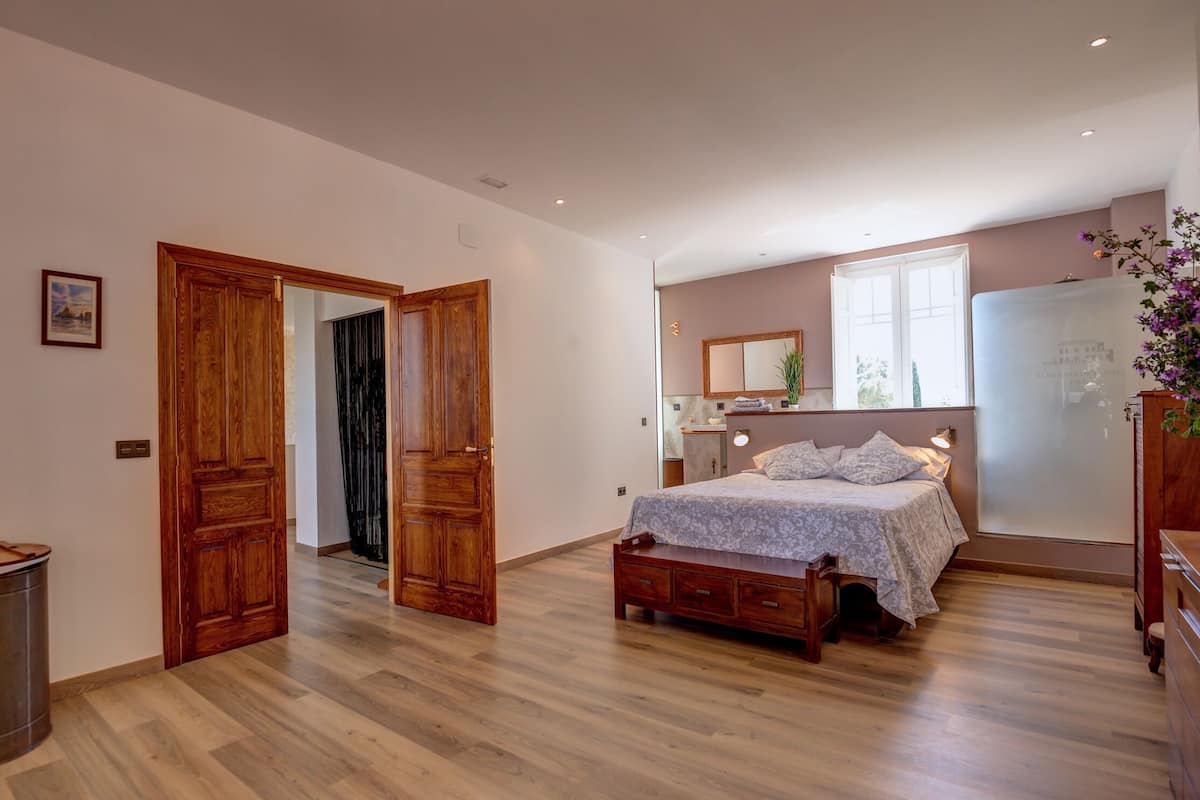 Une chambre à coucher avec un lit en bois, une armoire en bois, une petite table de chevet, un miroir et une fenêtre donnant sur l’extérieur.