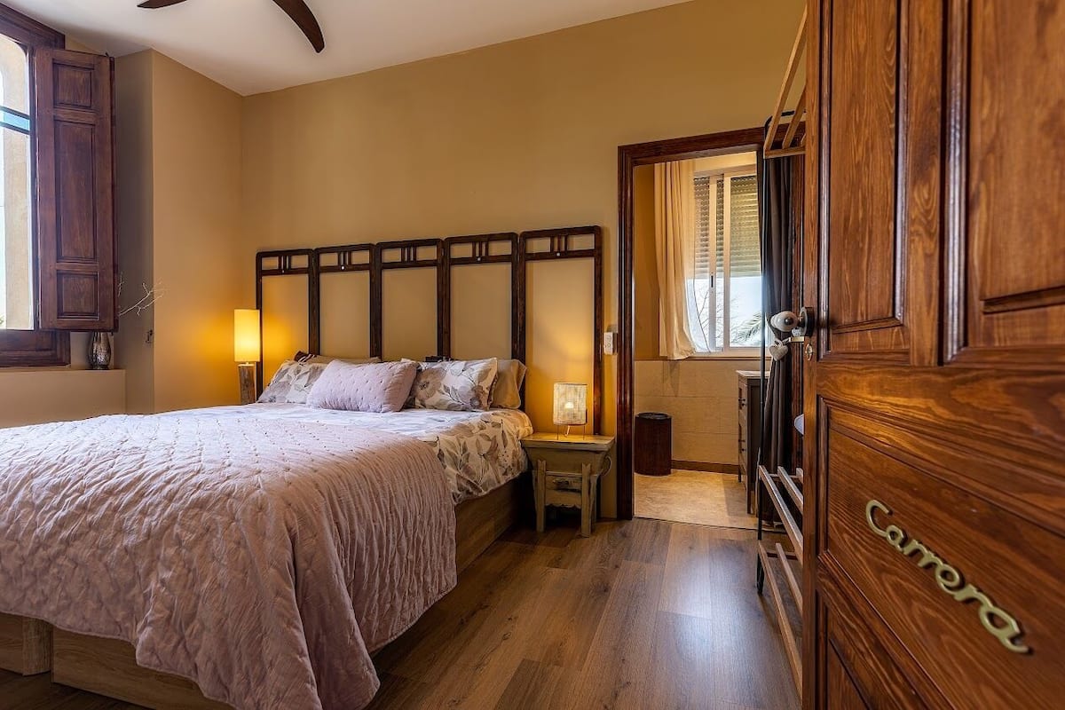 Une chambre à coucher avec un grand lit, des lampes de chevet, une tête de lit en bois, une armoire et une fenêtre avec des rideaux.
