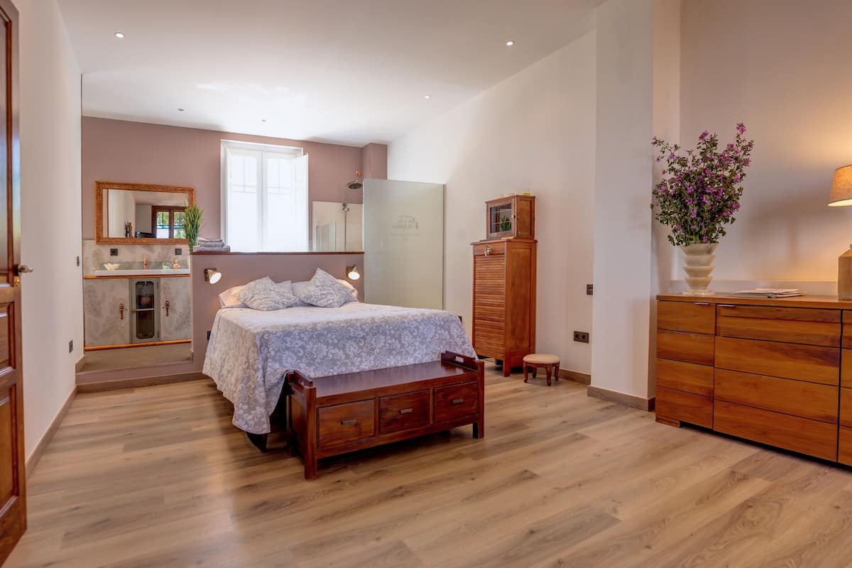 Une chambre à coucher avec un lit en bois, une commode, une coiffeuse avec un miroir et un petit tabouret.