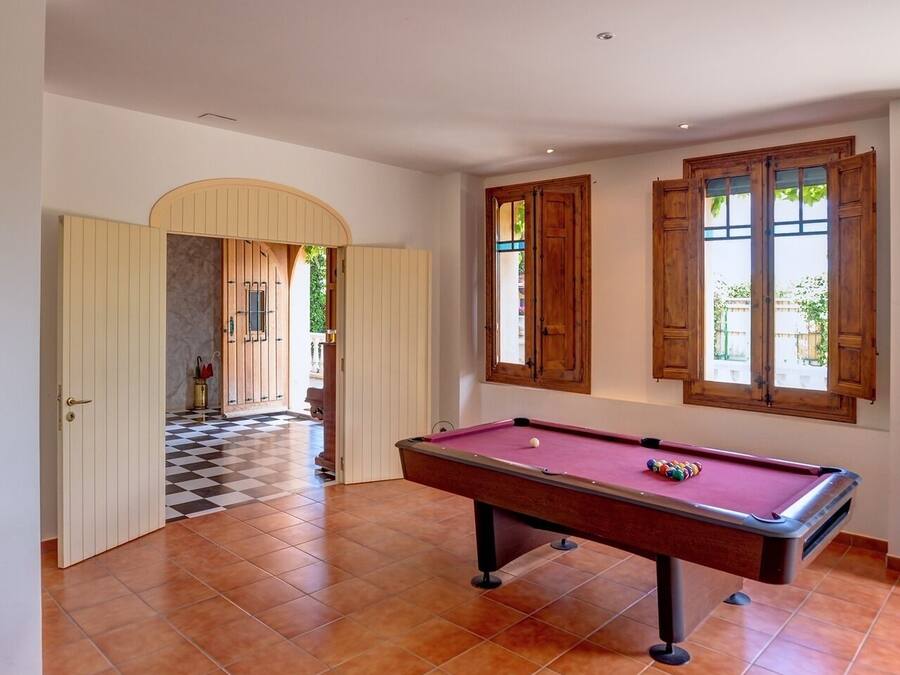 Uma sala de bilhar com mesa de bilhar, armários de madeira e chão xadrez.