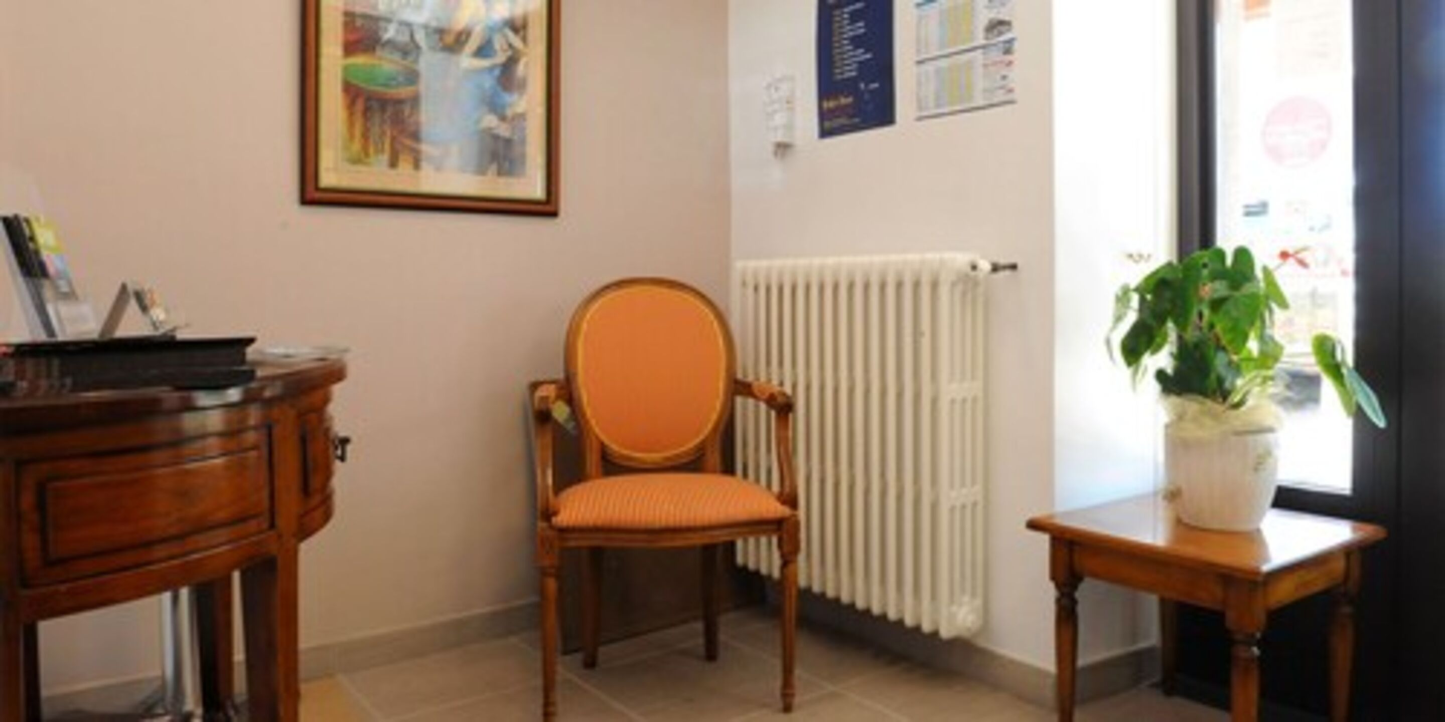 A room with a wooden chair, a small table with a plant, a radiator, and a framed picture on the wall.