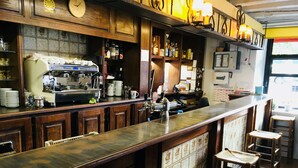 Una zona de bar con una máquina de café, estantes con botellas y un mostrador con taburetes.