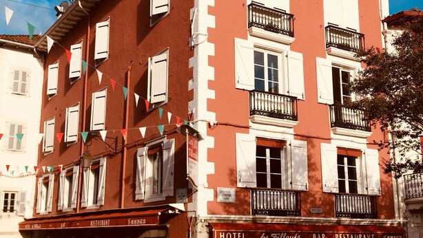 Un edificio rojo con contraventanas blancas y balcones, identificado como hotel y restaurante.
