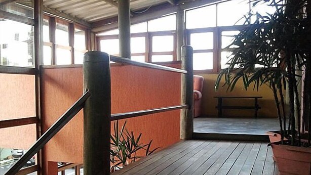 Un espacio al aire libre techado, con suelo de madera, barandilla de metal y un banco.