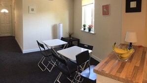 Un coin repas avec une table et des chaises, une fenêtre avec une plante et un saladier de bananes posé sur le comptoir.