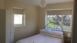 Un dormitorio con cama, ventana, puerta y mesita de noche con lámpara.