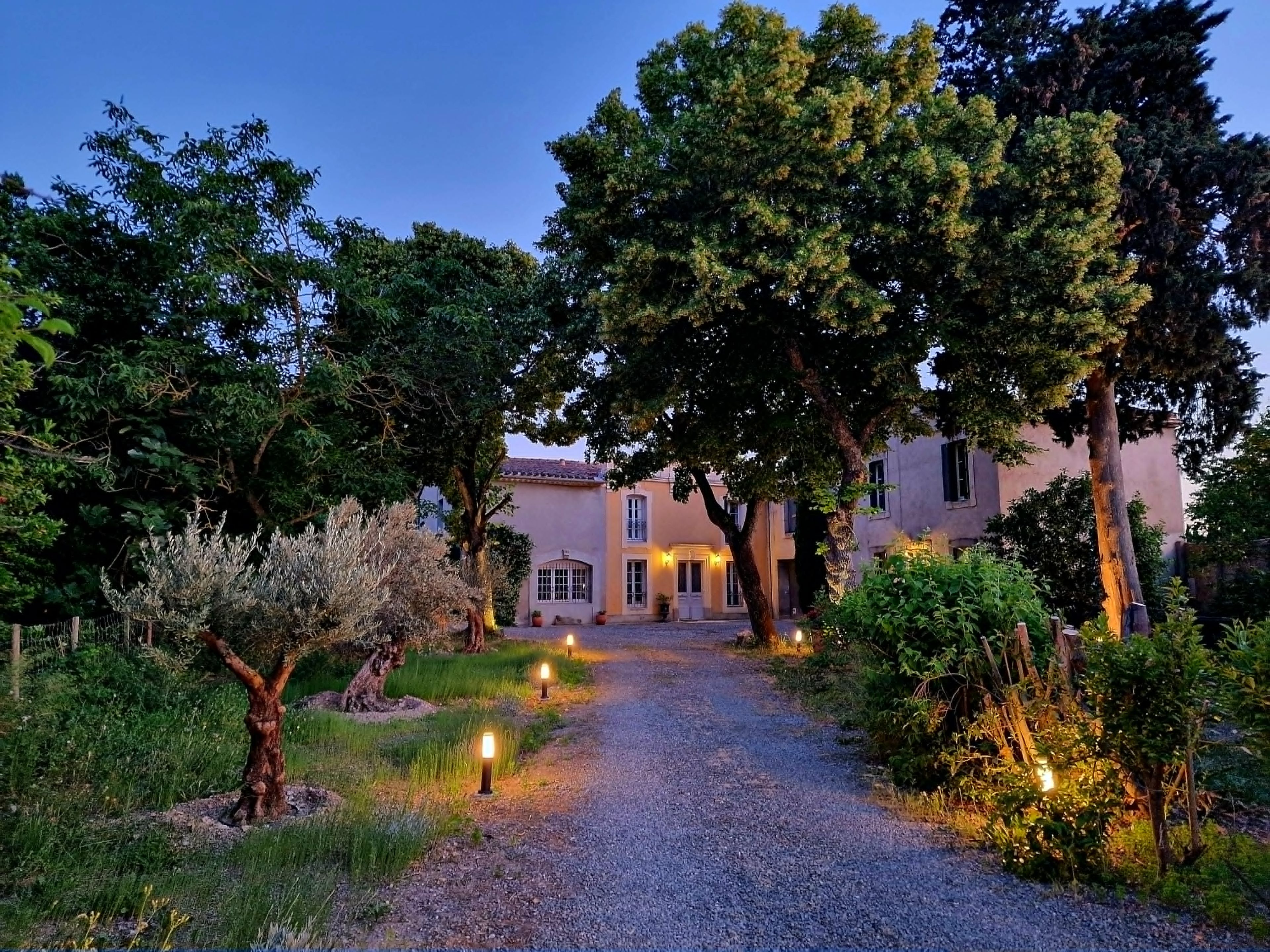 A gravel pathway leading to a building with a tiled roof, surrounded by trees and shrubs.