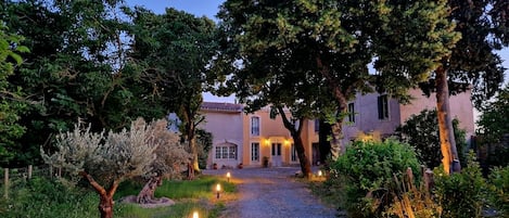 A gravel pathway leading to a building with a tiled roof, surrounded by trees and shrubs.