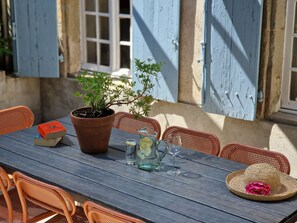 An outdoor dining area with a wooden table, chairs, a potted plant, a book, a glass pitcher, a glass, and a straw hat.