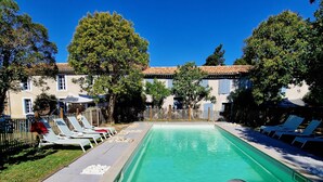A swimming pool with lounge chairs and a table with drinks and a book.