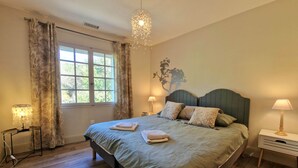 A bedroom with a large bed, two bedside tables, a chandelier, and a window with curtains.