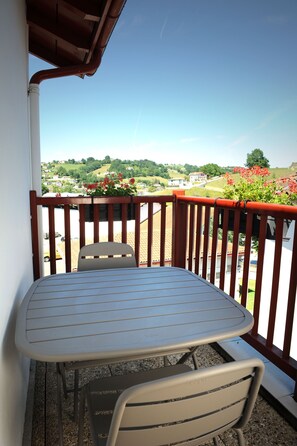 Ein Balkon mit Tisch und Stühlen, mit Blick auf eine reizvolle Landschaft mit Häusern und Grünflächen.
