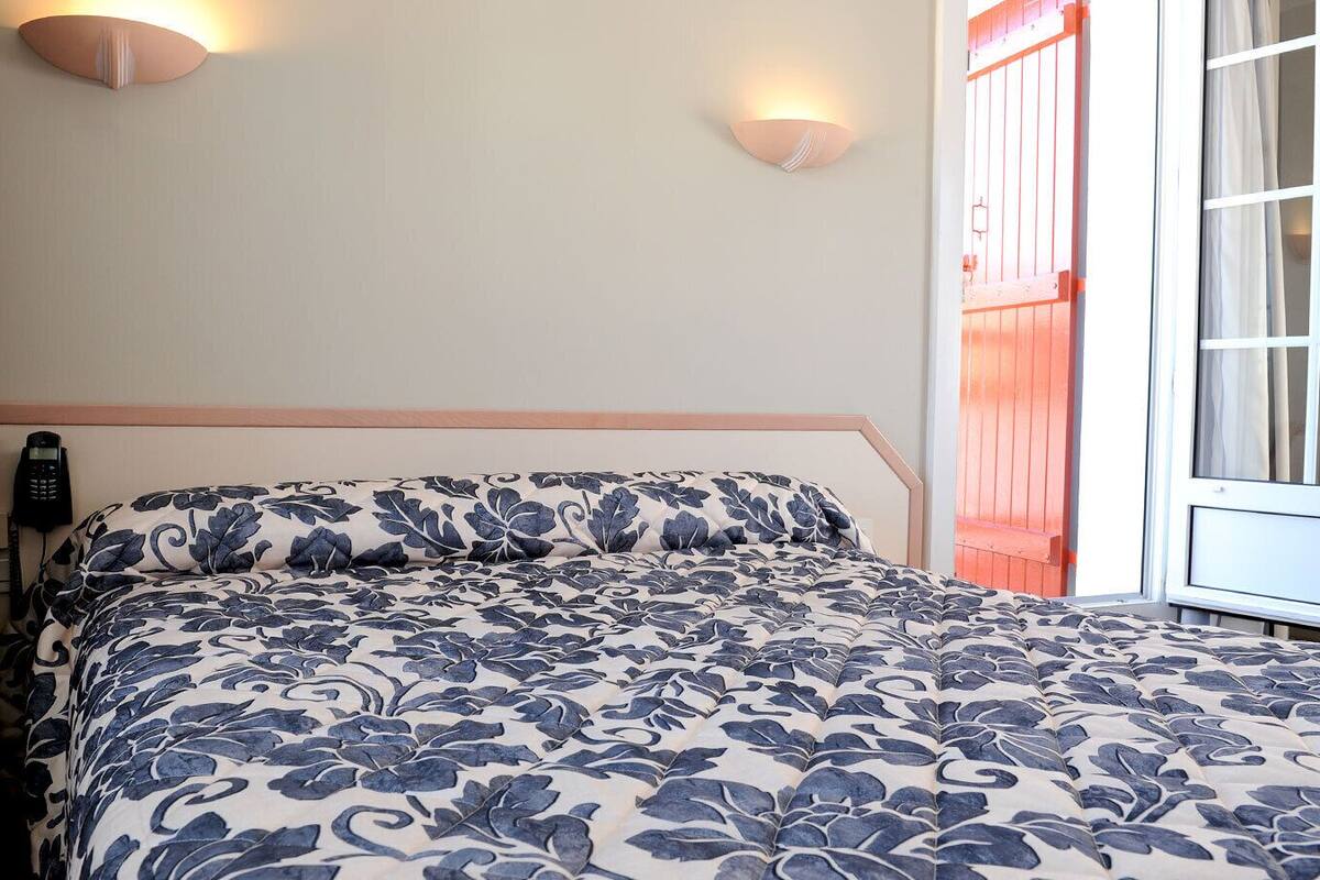 A bedroom with a bed, a telephone, and a window with curtains.
