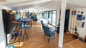 Um espaço amplo e interno com piso de madeira, área de bar e janelas grandes que oferecem vista para o exterior.