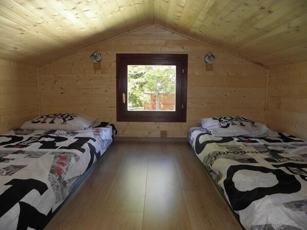 A small, wooden cabin room with two beds, a window, and a sloped ceiling. - Provence Roulottes Hébergement insolite (Barbentane)