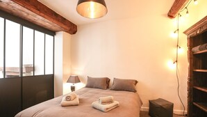 Una cama bien hecha con dos almohadas y dos toallas enrolladas, una lámpara de noche y un cabecero de madera con un estante.