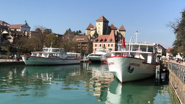Un canal con barcos amarrados, un castillo al fondo y un puente que une las dos orillas.