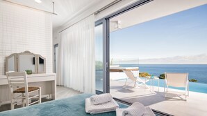 A bedroom with a large bed, a desk, and a view of the ocean through a sliding glass door. - Fiore Suites (Zakynthos)