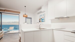 A modern kitchen with white cabinetry, a stainless steel sink, and a view of the ocean through a sliding glass door. - Fiore Suites (Zakynthos)