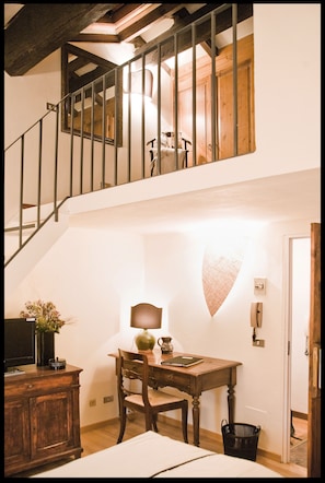 A room with a wooden desk, chair, and a small table with a lamp. There is a staircase with a railing leading to an upper level. - Cantarelli Bed & Breakfast (Reggio nell'Emilia)