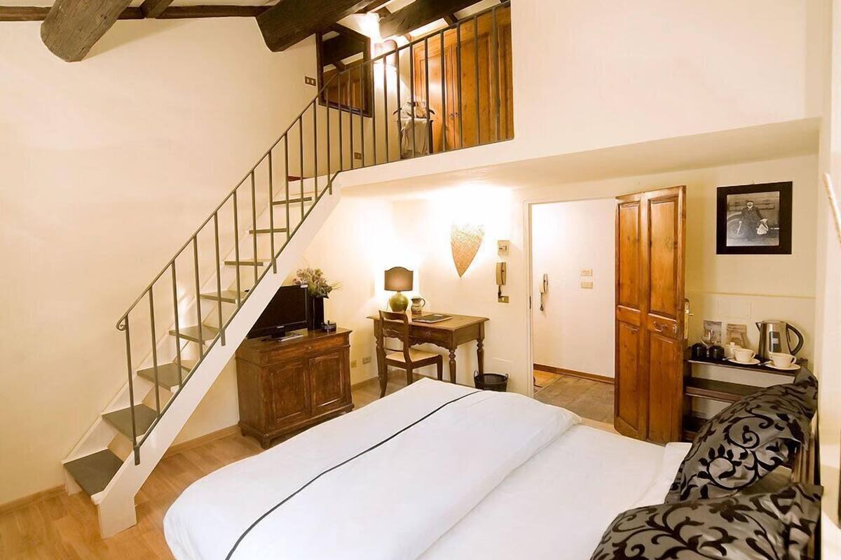 A bedroom with a bed, a desk, a chair, a staircase, and a wardrobe.