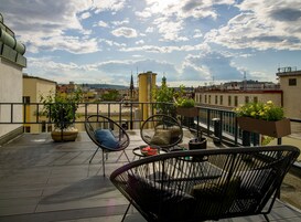 Una terrazza panoramica sul tetto con sedie in vimini, piante in vaso e vista sulla città.